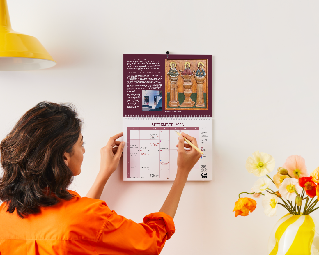 Woman looking at a calendar on a wall with a vase of flowers and yellow light fixture in the background.